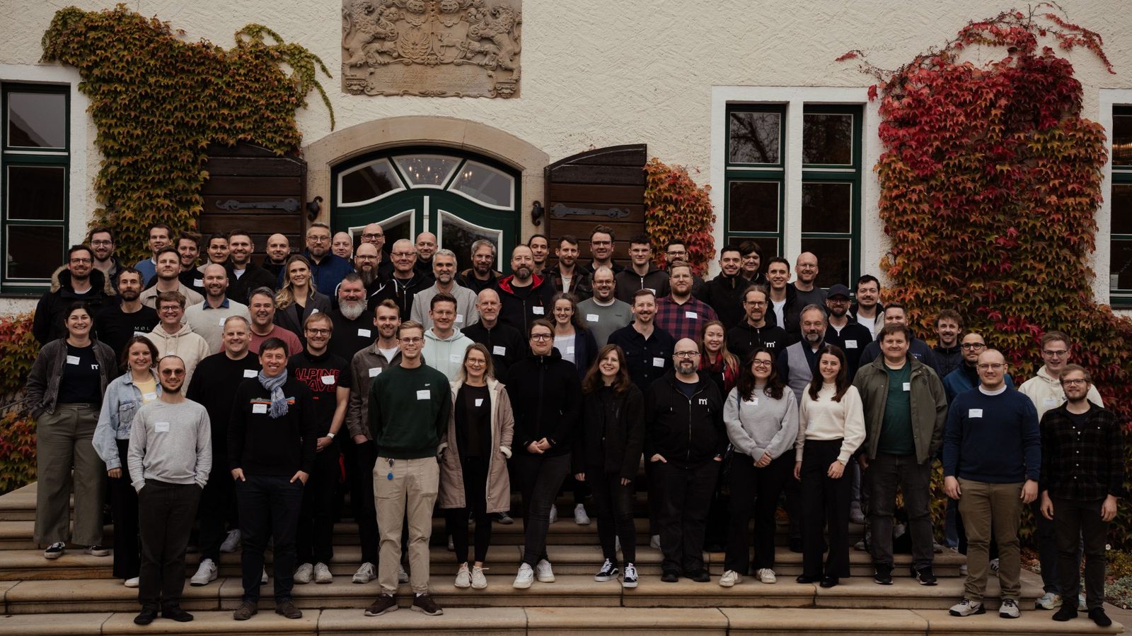 Gruppenfoto der Teilnehmenden des mittwald Agenturbeirats 2026 auf der Treppe vor Schloss Benkhausen, die Fassade mit herbstlich rotem und grünem Wein bewachsen