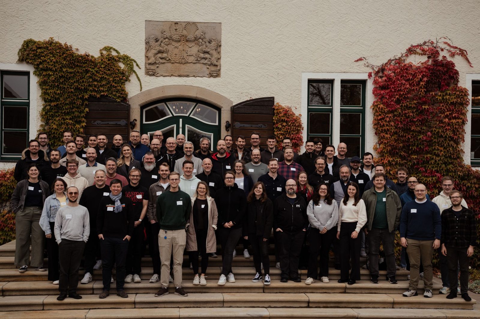 Gruppenfoto der Teilnehmenden des mittwald Agenturbeirats 2026 auf der Treppe vor Schloss Benkhausen, die Fassade mit herbstlich rotem und grünem Wein bewachsen